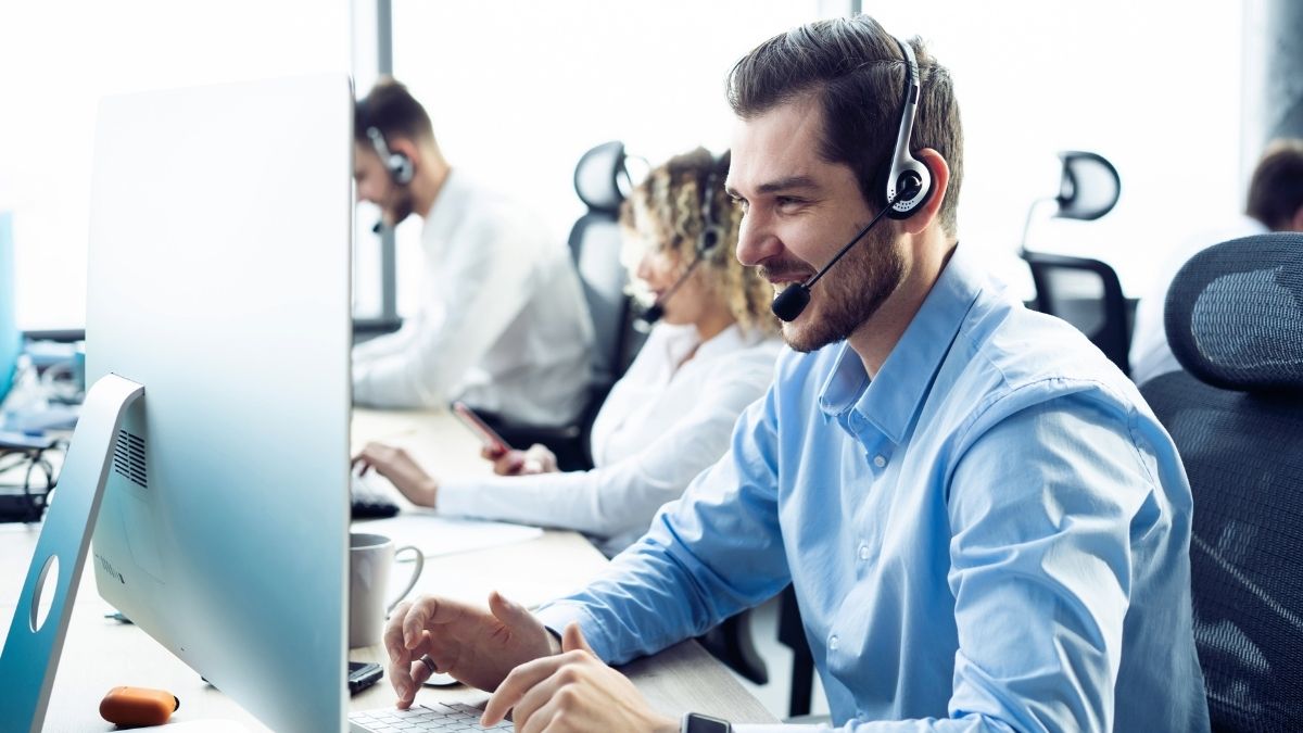 man on headset at computer with out of focus colleagues in background